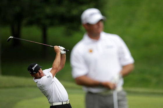 Graeme McDowell pega un golpe al fondo con Lee Westwood difuminado en primer plano.
