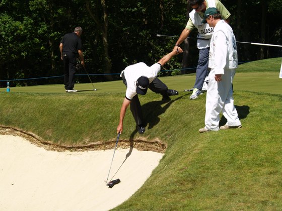 Olazábal trata de alcanzar la funda del putter en un búnker con la ayuda de su caddie Alex Larrazábal.
